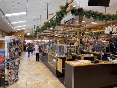 A spacious gift shop with wooden decor, showcasing various items and customers browsing among display cases.