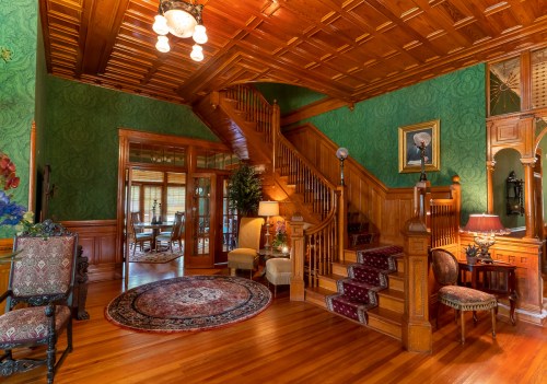 Elegant foyer with a wooden staircase, green wallpaper, ornate decor, and a vintage rug. Warm, inviting atmosphere.