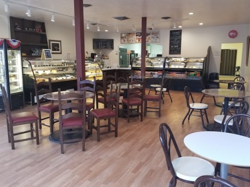 A cozy café interior with wooden tables and chairs, display cases filled with pastries, and a welcoming atmosphere.