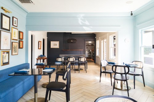 A bright, modern restaurant interior with blue walls, wooden floors, and stylish seating arrangements.