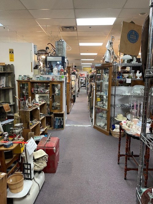 A narrow aisle in an antique store lined with shelves of vintage items and collectibles on either side.