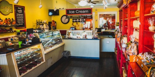 A colorful ice cream shop interior with display cases, a clock, and shelves filled with treats.
