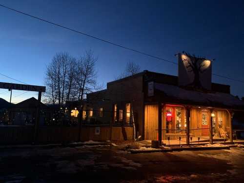 A rustic building with warm lights at dusk, featuring a tree mural and a sign that reads "Garden." Snow on the ground.