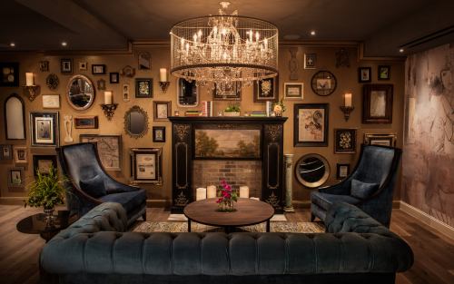 A cozy living room with a chandelier, framed art on the walls, and plush seating around a central table.