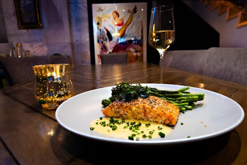 A plated salmon dish with asparagus and greens, accompanied by a glass of wine and a candle on a wooden table.