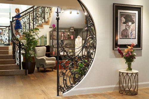 A stylish interior featuring a curved staircase, decorative railing, and a framed portrait with flowers on a side table.