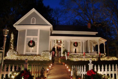A beautifully decorated house for the holidays, featuring wreaths, lights, and a welcoming front porch at night.