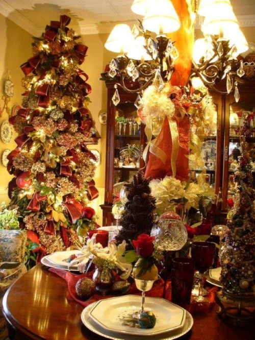 A festive dining room decorated for Christmas, featuring ornate trees, a chandelier, and a beautifully set table.
