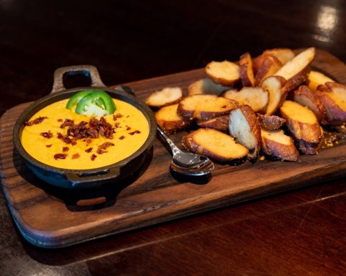 A cast iron skillet with creamy cheese dip topped with jalapeños and bacon, served with crispy toasted bread slices.