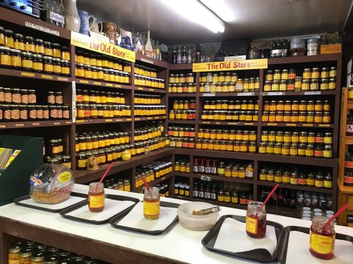 A cozy store interior filled with shelves of jars and preserves, with tasting samples on a counter in front.