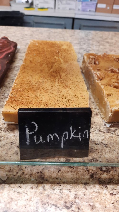 A block of pumpkin fudge with a sprinkle of spice, displayed behind a small black sign labeled "Pumpkin."