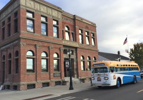 Historic brick building with large windows, featuring a blue and yellow bus parked in front.