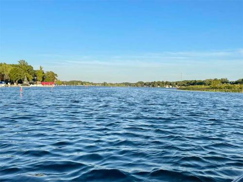 A serene view of a calm lake with clear blue water and trees lining the shore under a bright blue sky.