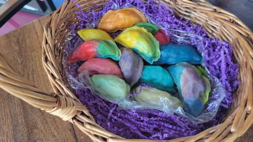 A woven basket filled with colorful, pastel-hued dumplings resting on purple shredded paper.