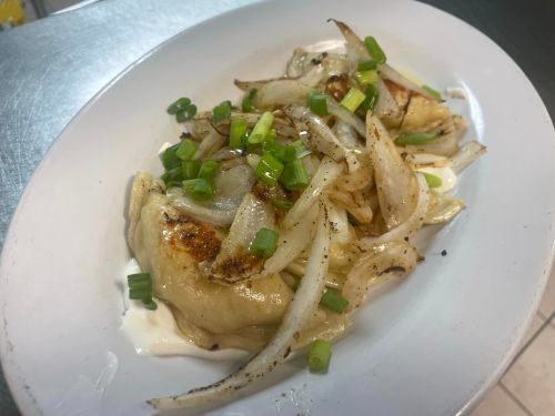 Plate of golden-brown dumplings topped with sautéed onions and green onions, served with a creamy sauce.