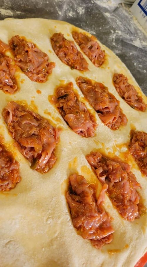 Dough with dollops of a reddish-brown filling, ready to be shaped or baked, on a floured surface.