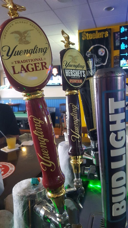 Close-up of beer taps featuring Yuengling Lager, Yuengling Hershey's Porter, and Bud Light in a bar setting.