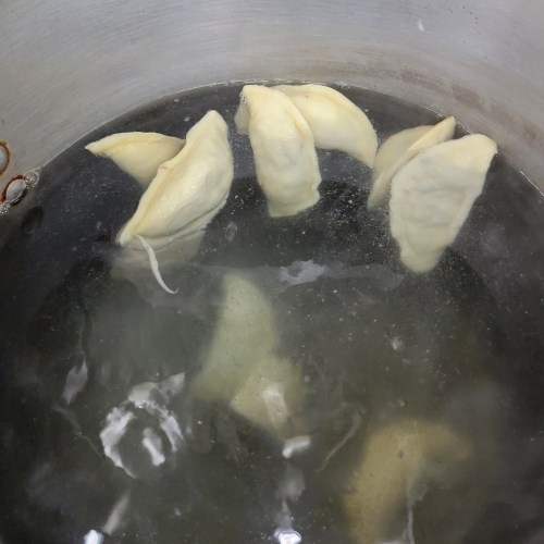 Dumplings boiling in a pot of water, partially submerged and floating.
