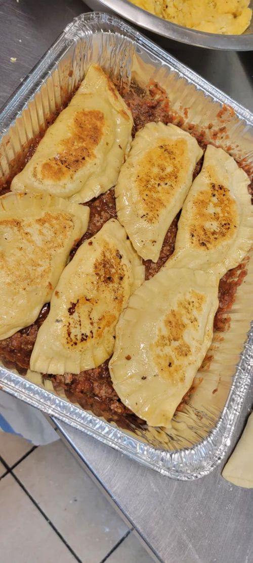A tray of golden-brown dumplings filled with meat, resting on a bed of sauce.