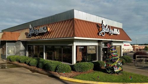 A restaurant with a brown metal roof and large windows, featuring a colorful holiday tree outside.