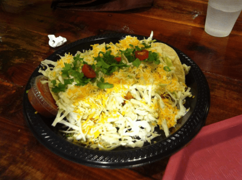 A black plate filled with shredded lettuce, cheese, diced tomatoes, and cilantro, accompanied by a small container of salsa.