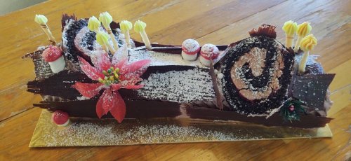 A beautifully decorated chocolate yule log cake with flowers, mushrooms, and festive details on a wooden table.