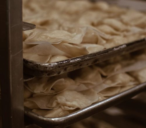 A close-up of stacked trays filled with uncooked dumplings in a kitchen setting.