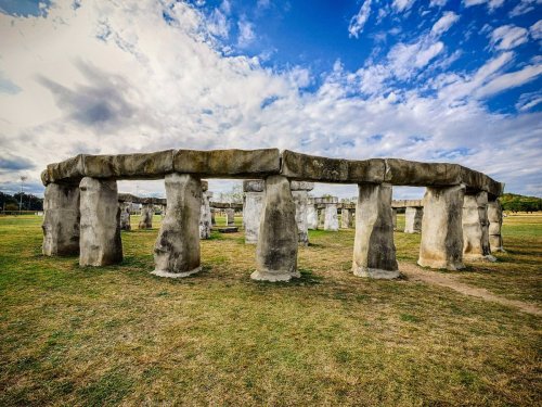 A stone circle with large upright stones and a horizontal lintel, set against a cloudy blue sky.