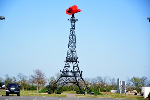 A replica of the Eiffel Tower topped with a large red cowboy hat, set against a clear blue sky.