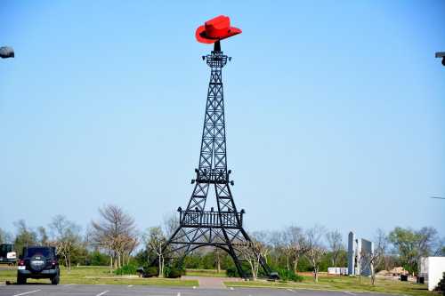 A replica of the Eiffel Tower topped with a large red cowboy hat, set against a clear blue sky.