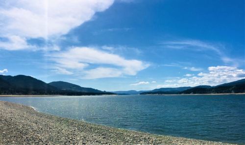 A serene lake surrounded by mountains under a bright blue sky with scattered clouds.