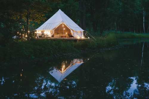 A cozy tent by a calm lake, illuminated by string lights, reflecting on the water at dusk.