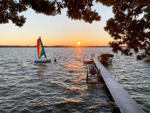 A colorful sailboat on a lake at sunset, with a dock and people enjoying the view.