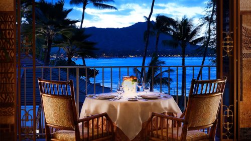 A romantic dining setup with two chairs and a table overlooking a serene ocean view at sunset.