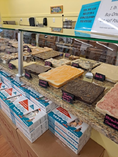 A display of various fudge flavors and boxes of taffy in a candy shop.
