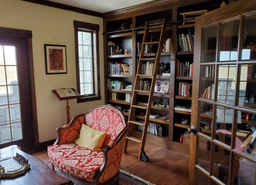 Cozy room with a red patterned chair, wooden ladder, and bookshelves filled with books and decor. Glass doors in view.