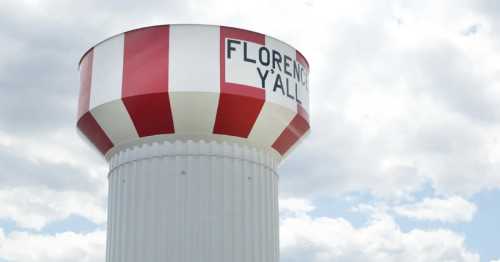 A water tower with red and white stripes, featuring the text "Florence Y'all" against a cloudy sky.