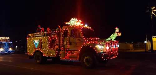 A brightly lit fire truck adorned with colorful lights and decorations, driving through a nighttime parade.