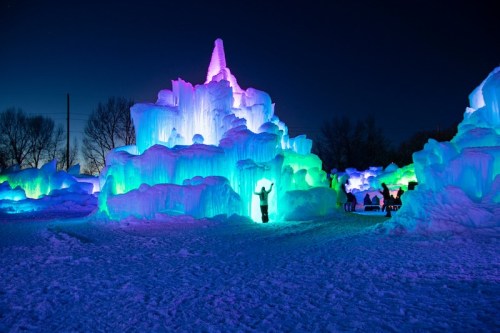 Colorful ice sculptures illuminated at night, with visitors exploring the vibrant, glowing formations.