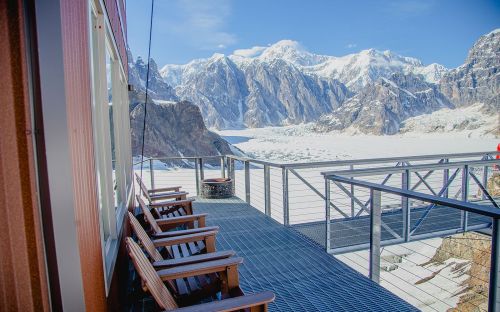 A scenic view from a deck overlooking a glacier and snow-capped mountains under a clear blue sky.