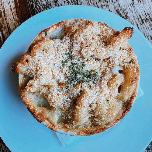 A golden-brown baked dish topped with breadcrumbs and herbs, served in a round dish on a light blue plate.