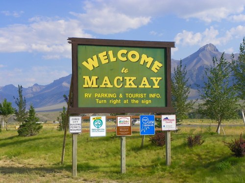 A large green sign reading "Welcome to Mackay" with directions for RV parking and tourist information, set against mountains.