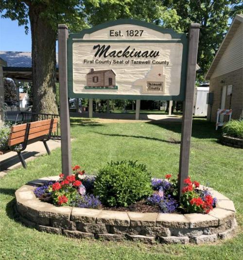 Sign for Mackinaw, established 1827, marking the first county seat of Tazewell County, surrounded by colorful flowers.