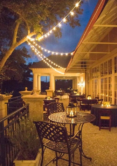Cozy outdoor dining area with string lights, tables, and candles, set against a twilight sky.
