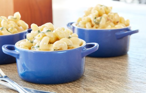 Three blue bowls filled with creamy macaroni and cheese, garnished with green herbs, on a wooden table.