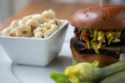 A close-up of a burger with toppings beside a bowl of macaroni salad on a plate.
