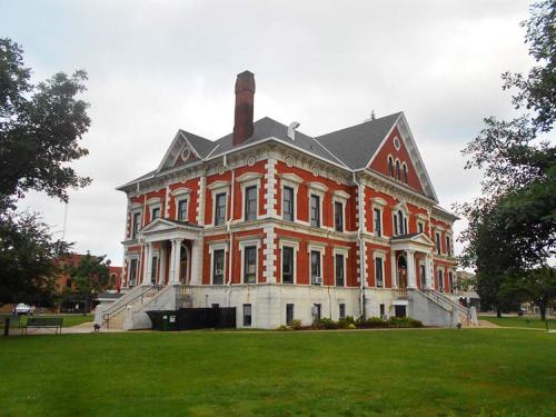 Historic brick building with ornate architecture, large steps, and a grassy area in front, under a cloudy sky.