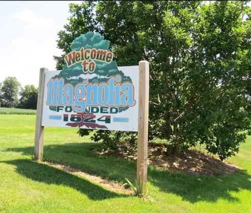 Welcome sign for Magnolia, established in 1824, surrounded by green grass and trees.