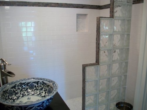 A modern bathroom featuring a glass block shower wall, white tiles, and a decorative bowl sink.