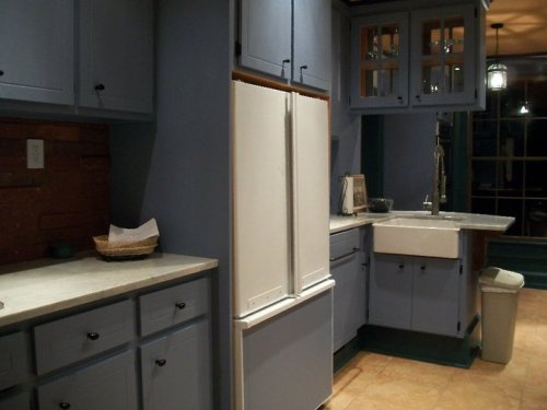 A cozy kitchen with blue cabinets, a white refrigerator, and a farmhouse sink, illuminated by soft lighting.